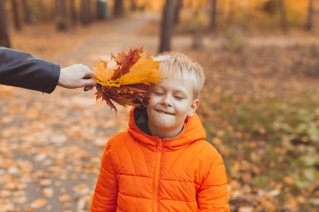 Porträt des glücklichen Kinderjungen in der orange Jacke im Herbstpark. Herbstsaison und Kinderkonzept