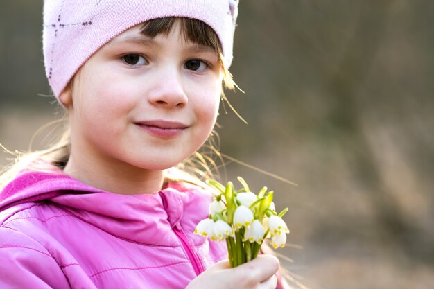 Porträt des glücklichen Kindermädchens, das Bündel der frühen Frühlingsschneeglöckchenblumen im Freien hält