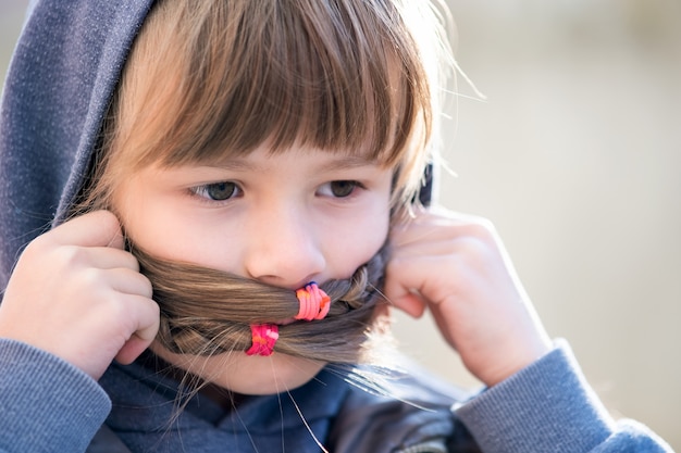 Porträt des glücklichen Kindermädchens mit Haarflechten in der warmen Kleidung im Herbst draußen.