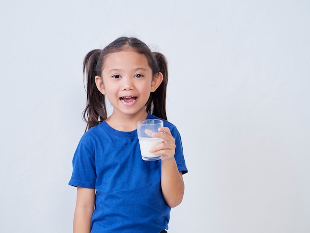 Porträt des glücklichen kleinen Mädchens mit Glas Milch auf Licht