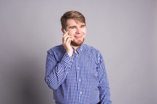 Porträt des glücklichen Mannes, der am Telefon über graue Wand spricht.