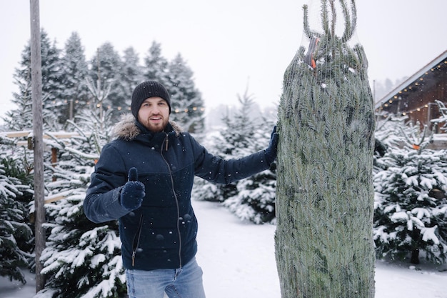Porträt des glücklichen Mannes trägt Weihnachtsbaum vom grünen Ladenmarkt der Öko-Bäume Tannenbaumverpackung