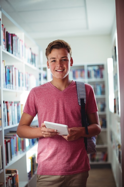 Porträt des glücklichen Schülers, der digitales Tablett in Bibliothek hält