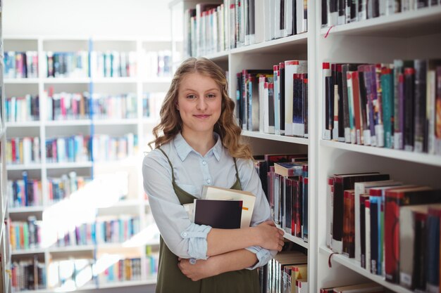 Porträt des glücklichen Schulmädchens, das Bücher in der Bibliothek hält