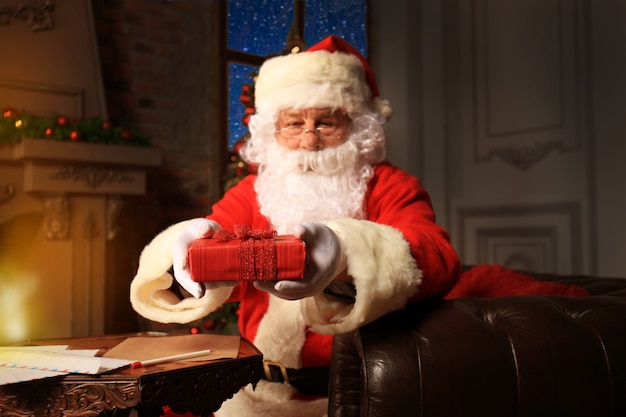 Porträt des glücklichen Weihnachtsmannes, der in seinem Zimmer zu Hause in der Nähe des Weihnachtsbaums sitzt und Weihnachtsbrief oder Wunschliste liest.