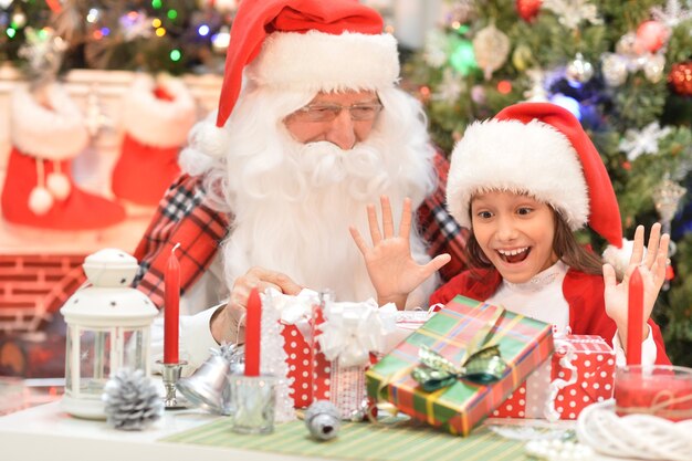 Porträt des glücklichen Weihnachtsmannes und des Mädchens in der Weihnachtsmütze mit Geschenken