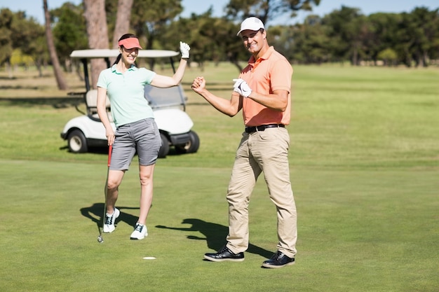 Porträt des Golfpaares in voller Länge, das Erfolg feiert