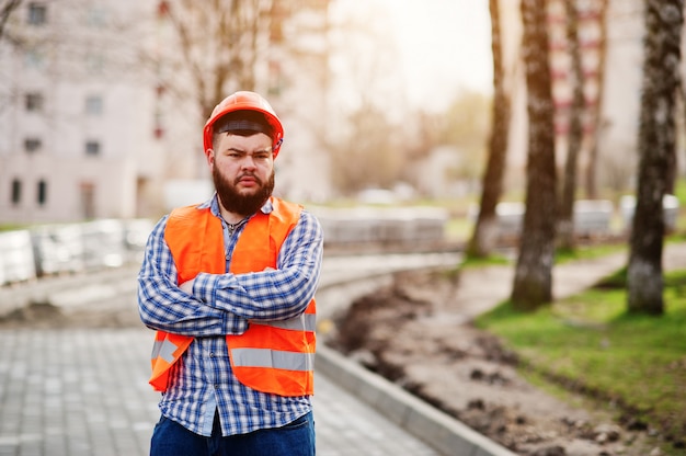 Porträt des groben Bartarbeitskraftmannklagenbauarbeiters im orange Sturzhelm der Sicherheit gegen Pflasterung.