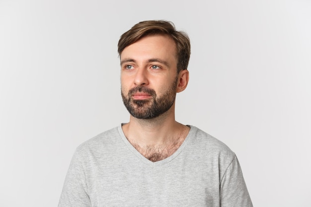 Porträt des gutaussehenden bärtigen Mannes im grauen T-Shirt, nachdenklich links schauend