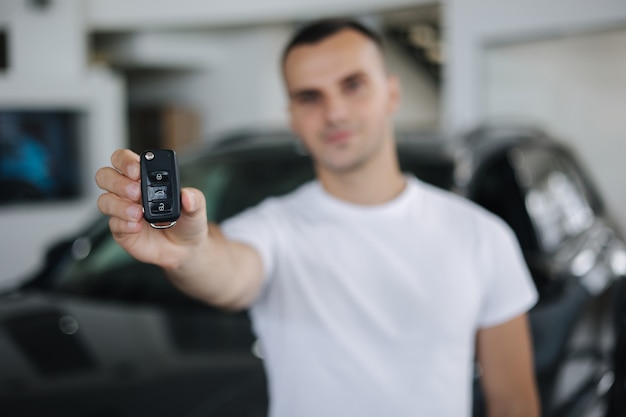 Porträt des handosom mannes im autohaus mann hält schlüssel von ihren neuen autoschlüsseln im fokus