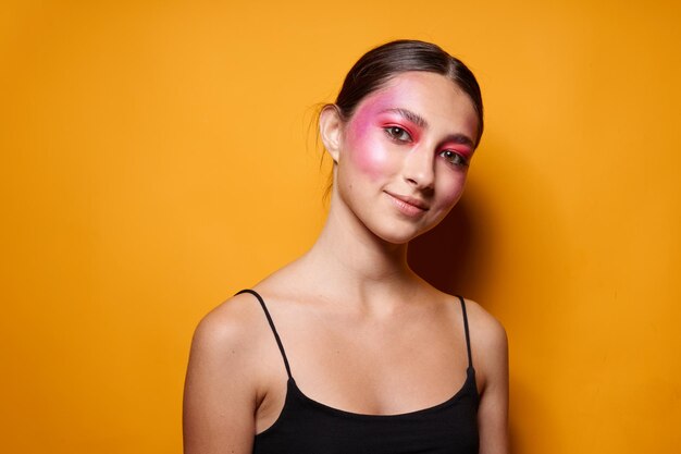 Porträt des hellen Make-ups der schönen jungen Frau, das den gelben Hintergrund des schwarzen Trikots unverändert aufwirft