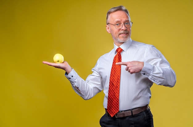 Porträt des hübschen älteren Mannes, der zur Kamera aufwirft. Mann hält einen Apfel in der Hand. Getrennt über gelbem Hintergrund.