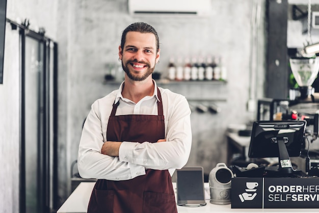 Porträt des hübschen bärtigen Barista-Mannes Kleinunternehmer, der hinter der Thekenbar in einem Café lächelt