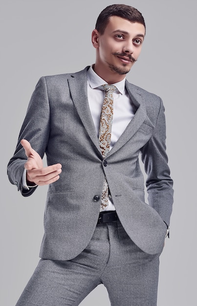 Porträt des hübschen jungen überzeugten arabischen Geschäftsmannes mit grauem vollem Anzug des fantastischen Schnurrbartes in Mode