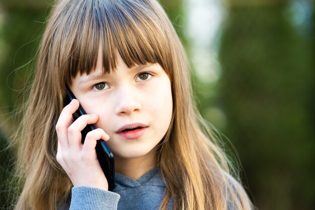 Porträt des hübschen Kindermädchens mit den langen Haaren, die auf Handy sprechen. Kleines weibliches Kind, das mit Smartphone kommuniziert. Kommunikationskonzept für Kinder.