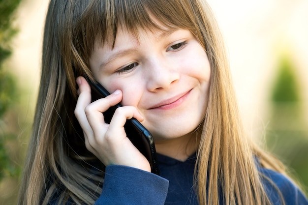 Porträt des hübschen Kindermädchens mit den langen Haaren, die auf Handy sprechen. Kleines weibliches Kind, das mit Smartphone kommuniziert. Kommunikationskonzept für Kinder.