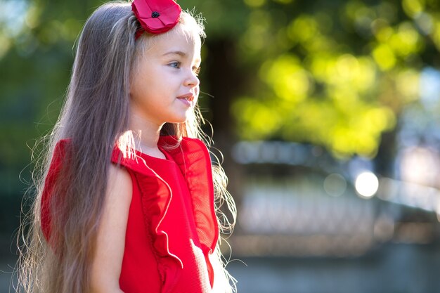 Porträt des hübschen modischen Kindermädchens im roten Kleid, das warmen sonnigen Sommertag genießt.