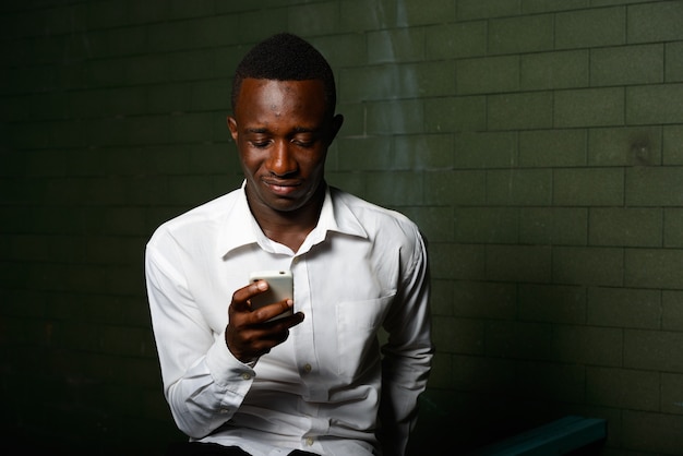Porträt des jungen afrikanischen Geschäftsmannes in der Dunkelheit gegen gegen Ziegelmauer in der Nacht