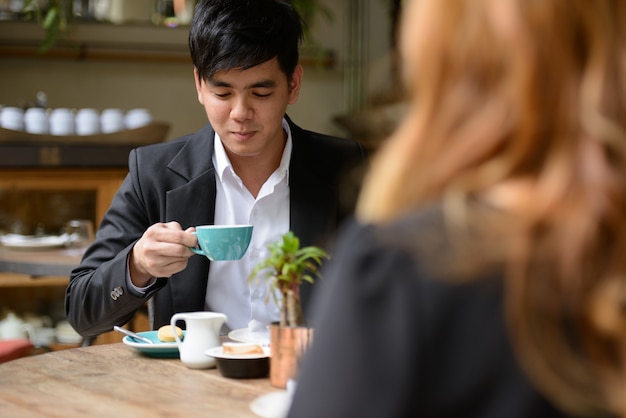 Porträt des jungen asiatischen Geschäftsmannes und der jungen asiatischen Geschäftsfrau, die zusammen im Café entspannen