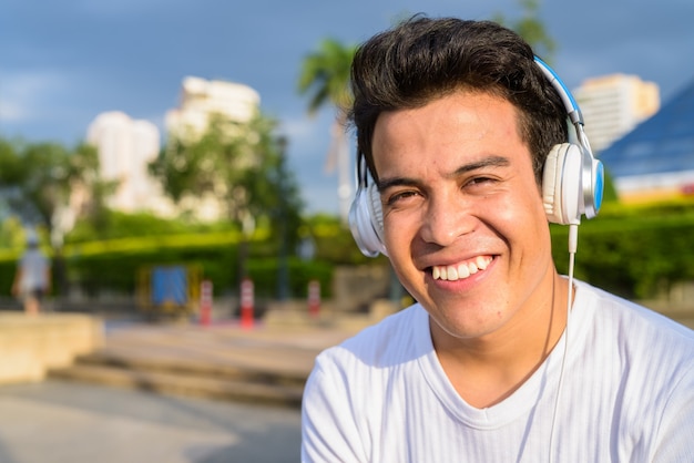 Porträt des jungen asiatischen Mannes, der Musik beim Entspannen am Park in Bangkok, Thailand hört