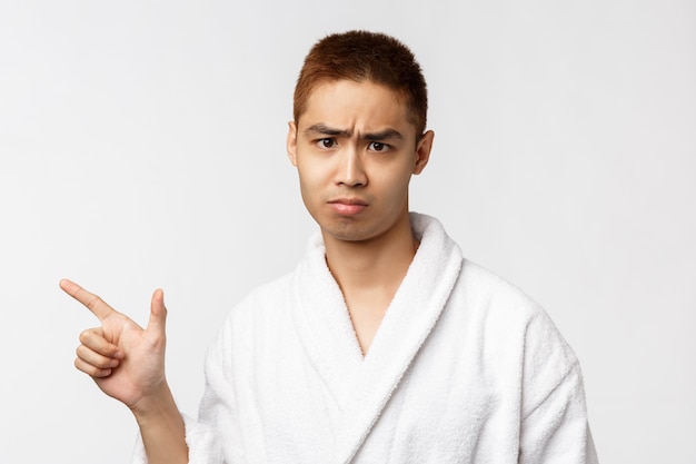 Porträt des jungen asiatischen Mannes im Bademantel, der Geste zeigt. Nach dem Duschen