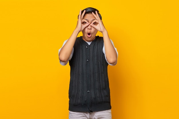 Porträt des jungen asiatischen mannes machen brillenmaske mit den fingern über den augen auf gelbem hintergrund