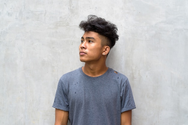 Porträt des jungen asiatischen Mannes mit lockigem Haar auf Betonwand im Freien