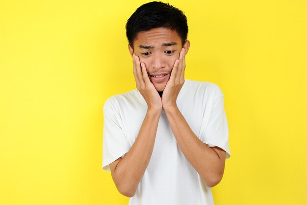 Porträt des jungen asiatischen Teenagers unglücklich verängstigter Mann, isoliert auf gelbem Hintergrund