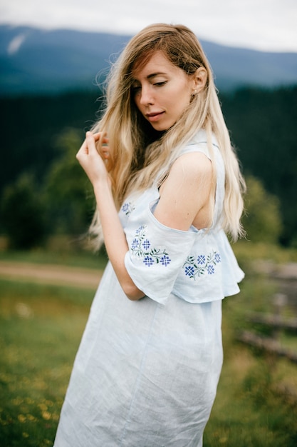 Porträt des jungen attraktiven eleganten blonden Mädchens im blauen romantischen Kleid, das über Landschaft aufwirft