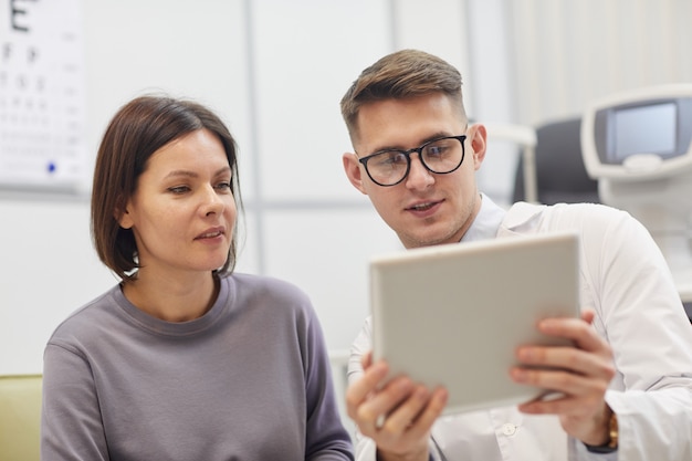 Porträt des jungen Augenarztes unter Verwendung der digitalen Tablette unter Rücksprache mit der Patientin