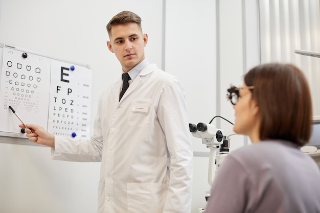 Porträt des jungen Augenoptikers, der auf Sichtkarte zeigt