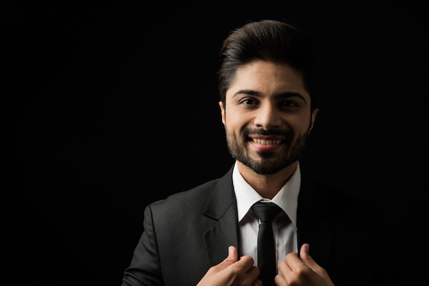 Porträt des jungen bärtigen indischen Geschäftsmannes vor schwarzem Hintergrund, stimmungsvolle Beleuchtung