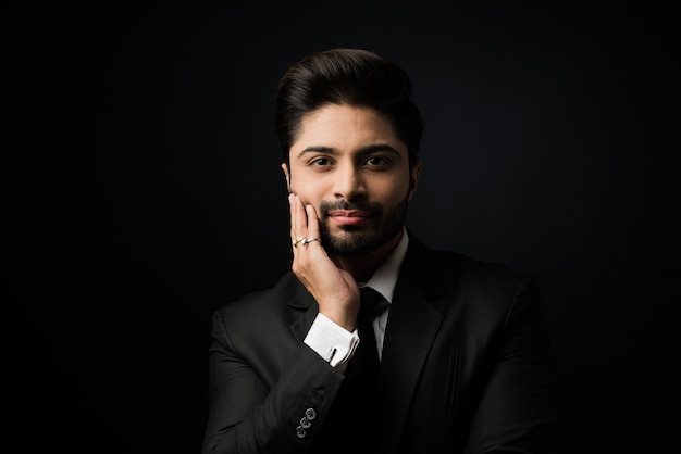 Porträt des jungen bärtigen indischen Geschäftsmannes vor schwarzem Hintergrund, stimmungsvolle Beleuchtung