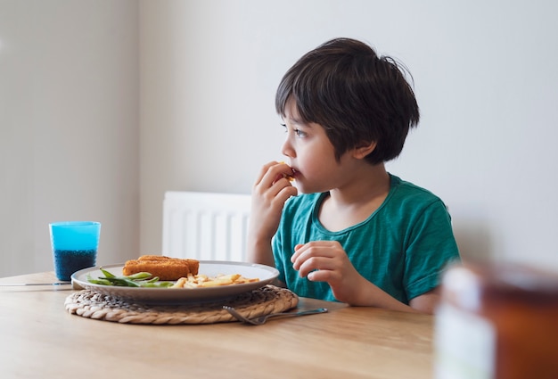 Porträt des Jungen, der hausgemachten Fischstäbchen und Pommes Frites für Sonntagabendessen zu Hause hat