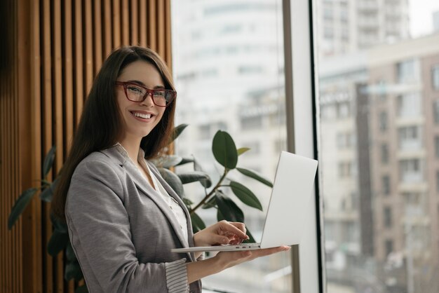 Porträt des jungen erfolgreichen Managers unter Verwendung des Laptops, der im Büro arbeitet