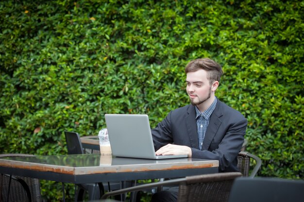 Porträt des jungen Geschäftsmannes, der Laptop in der modernen Kaffeestube im Freien verwendet