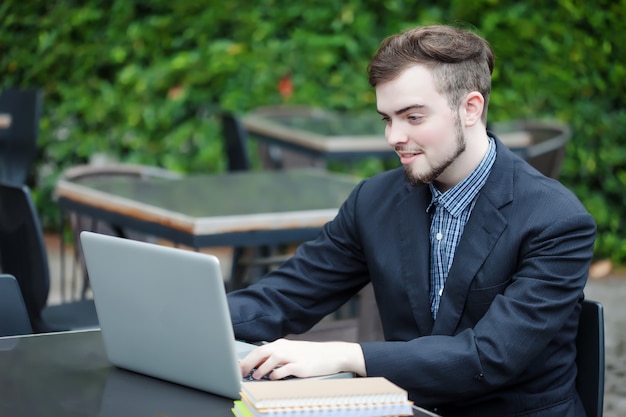 Porträt des jungen Geschäftsmannes, der Laptop in der modernen Kaffeestube im Freien verwendet