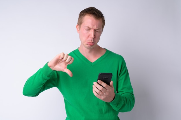 Porträt des jungen gestressten Mannes, der Telefon benutzt und schlechte Nachrichten erhält