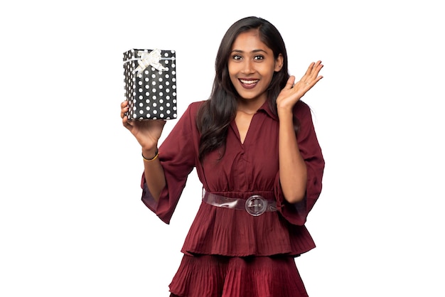 Porträt des jungen glücklichen lächelnden Mädchens im roten Kleid, das mit Geschenkbox auf weißem Hintergrund hält und aufwirft