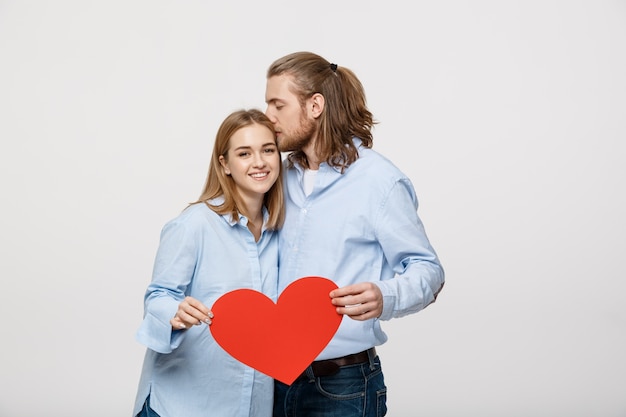 Porträt des jungen glücklichen Paars in der Liebe, die rotes Papierherz hält.