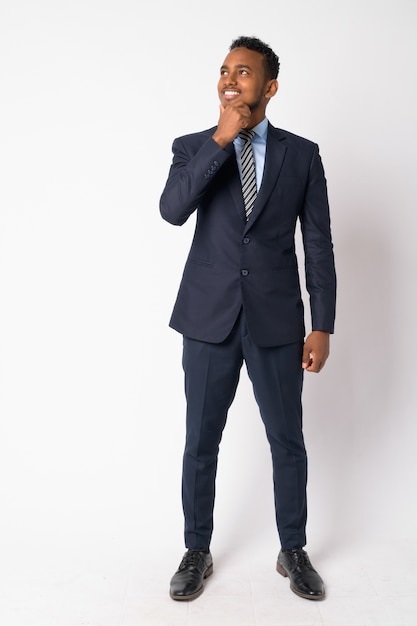 Porträt des jungen gutaussehenden afrikanischen Geschäftsmannes, der Anzug gegen weiße Wand trägt
