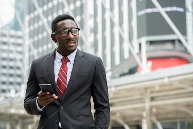 Porträt des jungen gutaussehenden afrikanischen Geschäftsmannes im Anzug gegen Ansicht des modernen Gebäudes in der Stadt im Freien