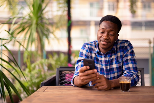 Porträt des jungen gutaussehenden afrikanischen Mannes, der am Kaffeehaus entspannt