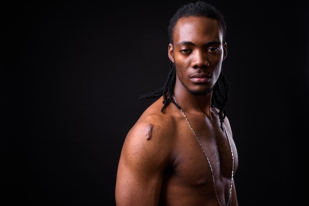 Porträt des jungen gutaussehenden afrikanischen Mannes mit Dreadlocks ohne Hemd auf Schwarz