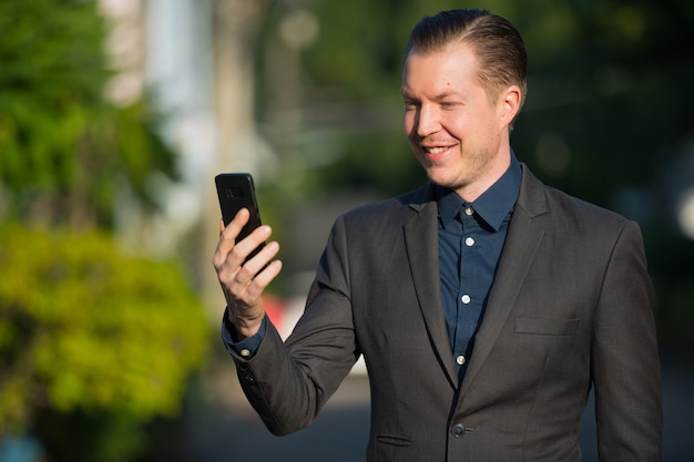 Porträt des jungen gutaussehenden Geschäftsmannes im Anzug mit blonden Haaren in den Straßen draußen