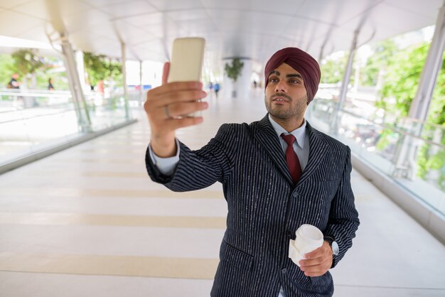 Porträt des jungen gutaussehenden indischen Sikh-Geschäftsmannes, der Turban trägt, während die Stadt Bangkok, Thailand erkundet