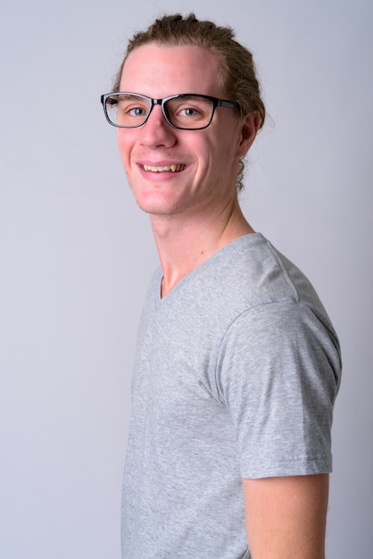 Porträt des jungen gutaussehenden Mannes, der Brillen mit den Haaren gegen weiße Wand gebunden trägt