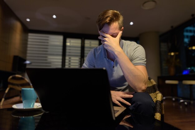 Porträt des jungen gutaussehenden Mannes unter Verwendung des Laptops im Wohnzimmer