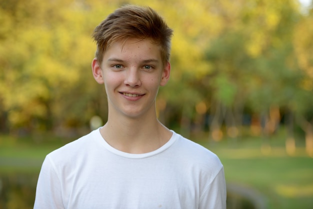 Foto porträt des jungen gutaussehenden teenagers, der sich im park draußen entspannt