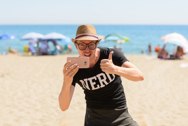 Porträt des jungen gutaussehenden Touristenmannes als Nerd am Strand in Spanien